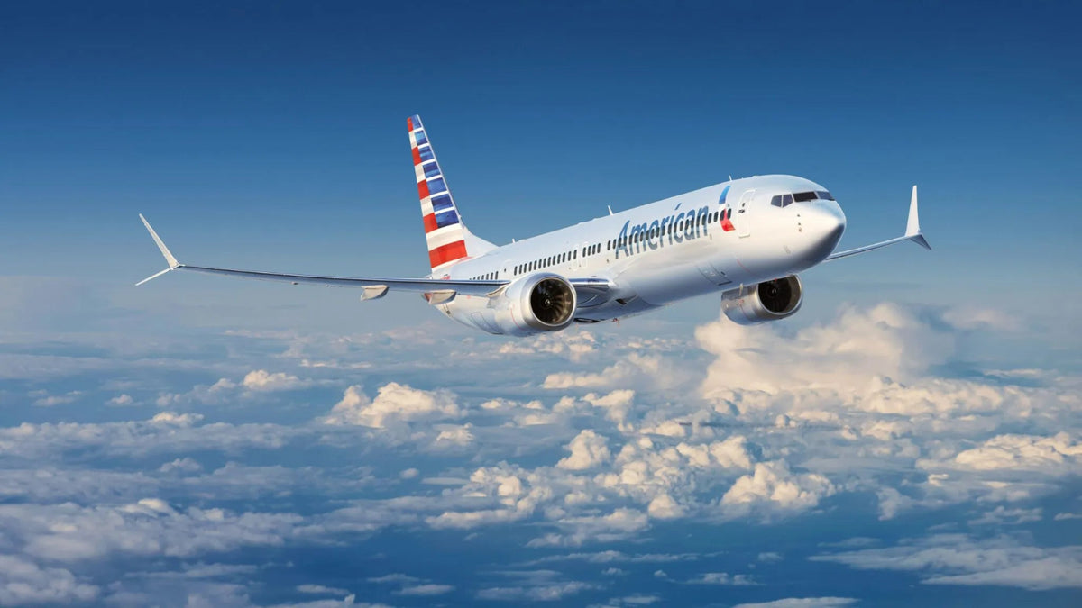 An American Airlines passenger jet flying through a blue sky with scattered white clouds below.